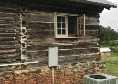 A log cabin with bricks on the lower half showcasing a window, power, and an AC unit