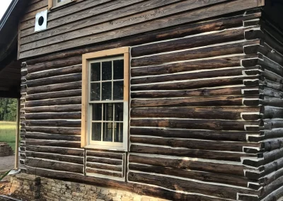 Stained log cabin with a large window and two small windows
