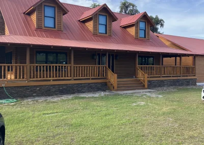Painted log cabin with wrap around deck, red roof, and new windows