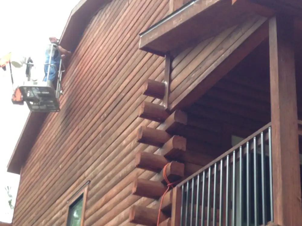 Crew member on a lift working on the upper logs of a dark-stained log home