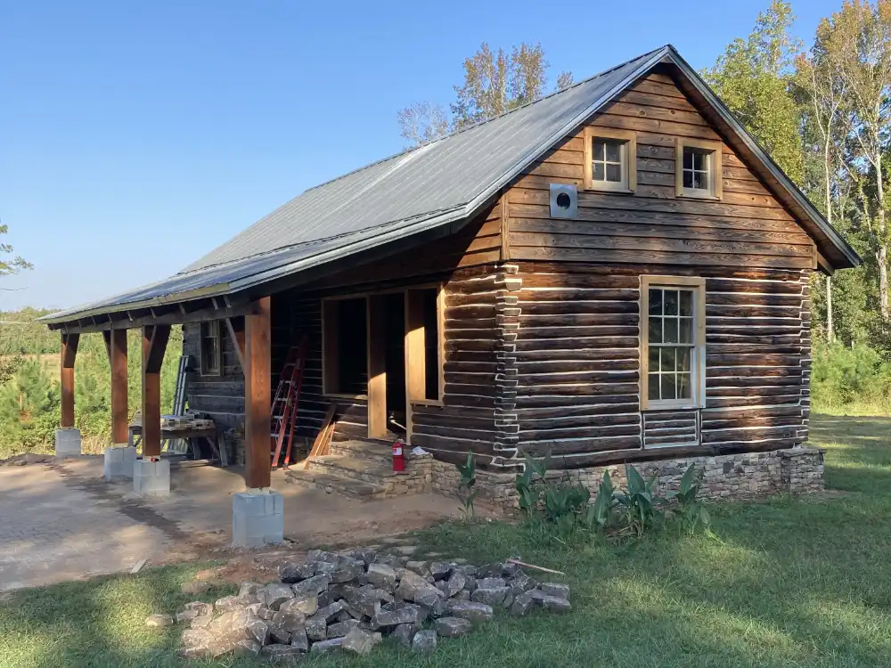 Weathered hewn log cabin with a front porch and stones stacked in the yard