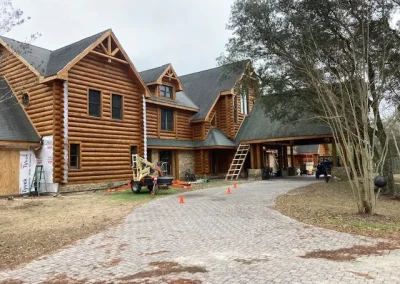 Large multi-gable log home with a ladder and lift staged on the paver driveway