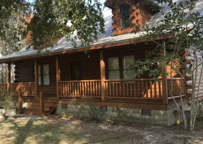 Log home with a front porch and dormer under shade trees