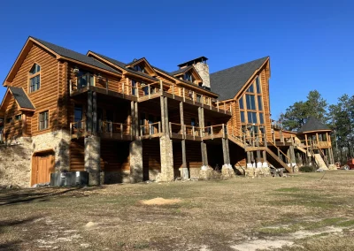 Large log lodge after exterior restoration, with fresh golden stain, stone piers and multi-level decks
