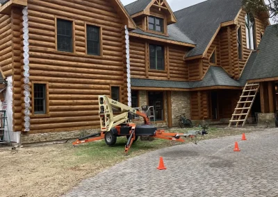 Log home with a paver driveway, safety cones and a lift staged for exterior work