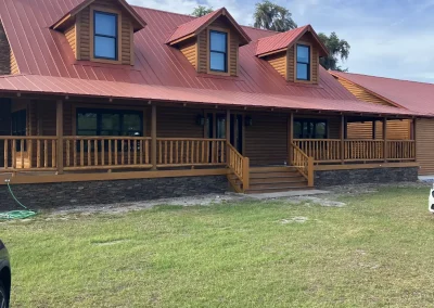 Log home with a red metal roof, three dormers and a wraparound porch