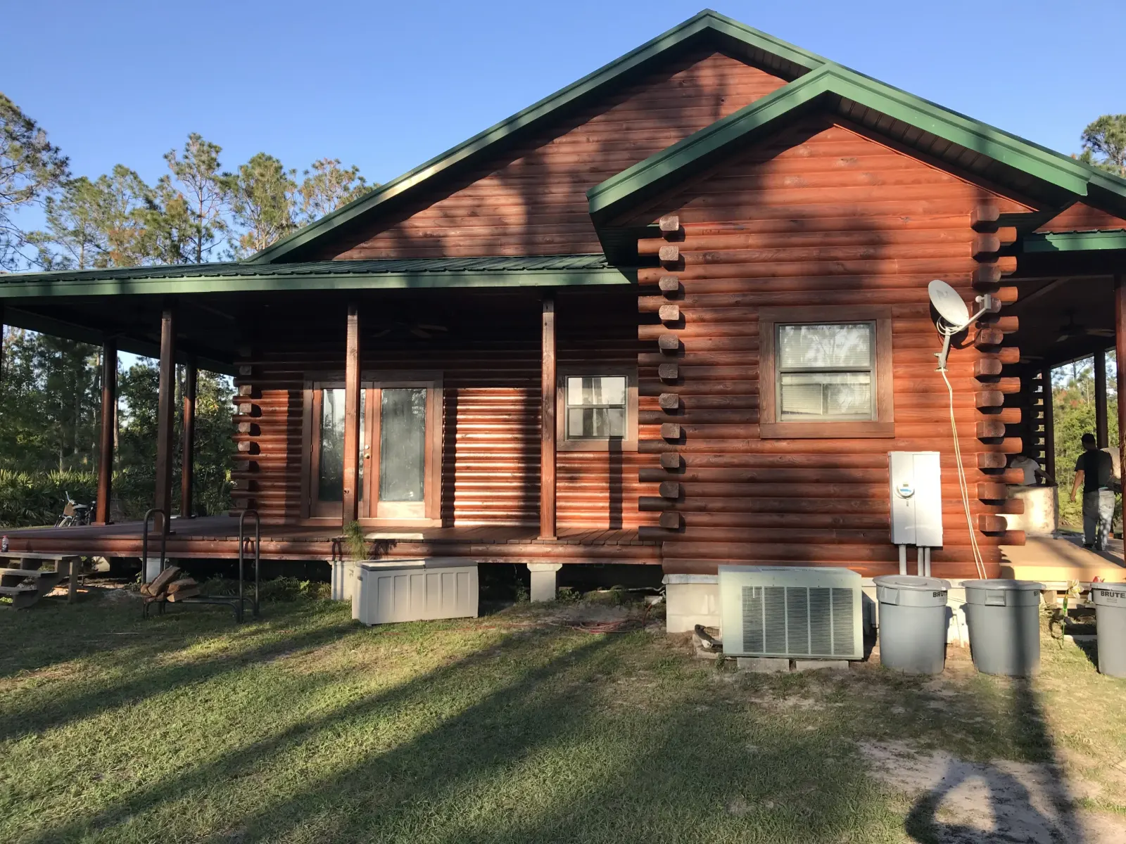 Red-stained log home with a green metal roof and wraparound porch