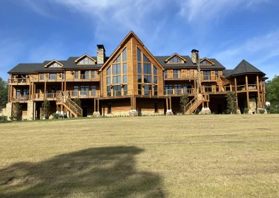 Rear of a large log lodge with a full-height glass gable and wraparound decks