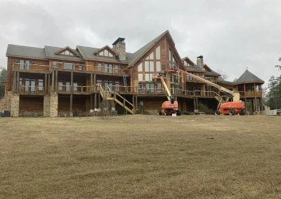 Two boom lifts set up behind a large log lodge during exterior restoration