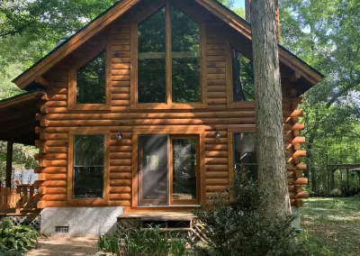 Prow-front log home with tall gable windows and a golden stain, set among trees