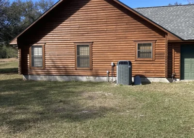 Stained log home with a gray shingle roof, seen from the side yard