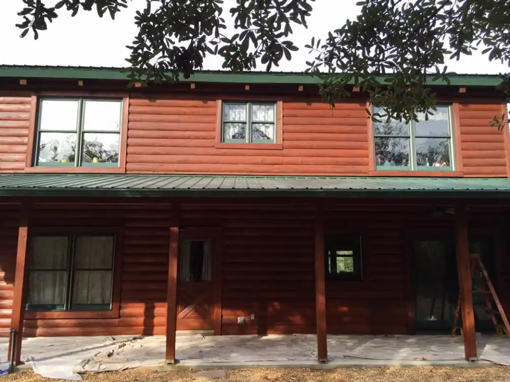 Two-story red-stained log home with a green metal roof and covered front porch