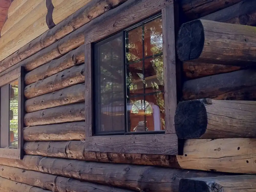 Close-up of weathered round logs, a window and protruding log ends at a corner